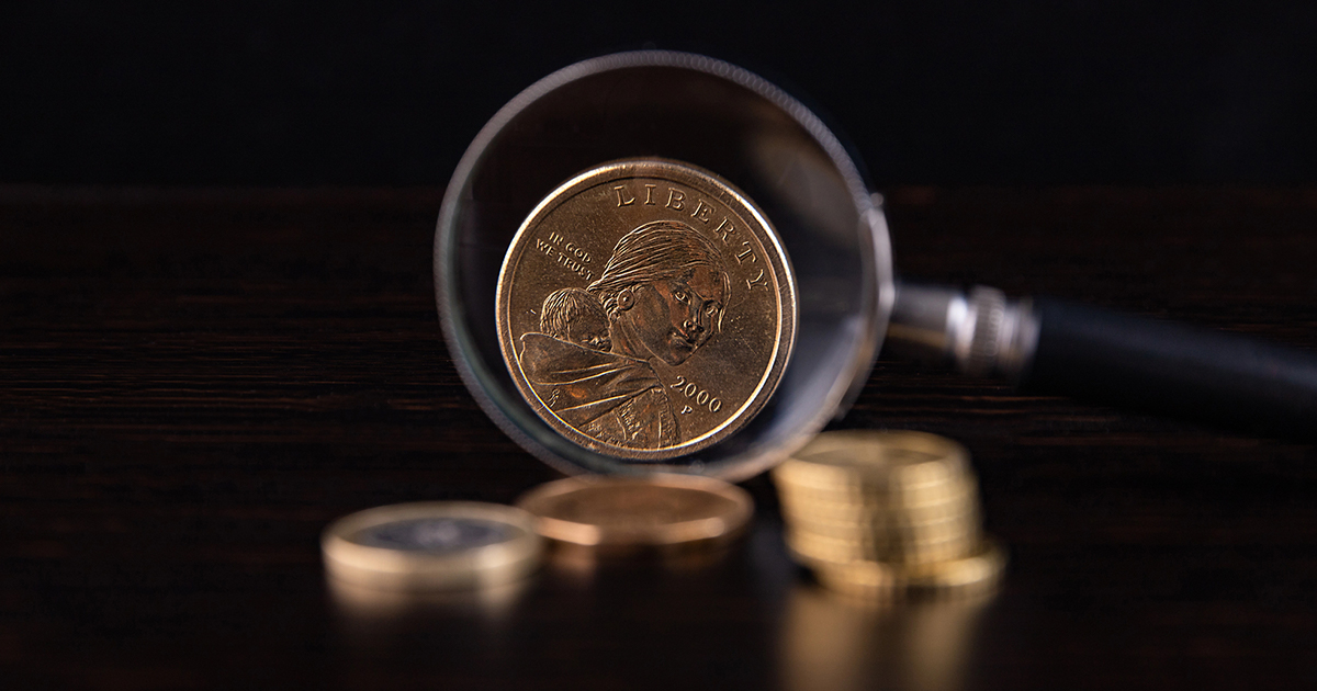 A magnifying glass rests on a gold coin, highlighting its intricate details and surface texture.